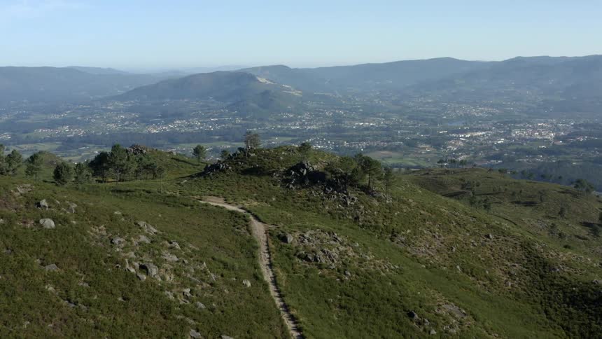 A dirt road runs along the slope of a steep hill overlooking a neighborhood