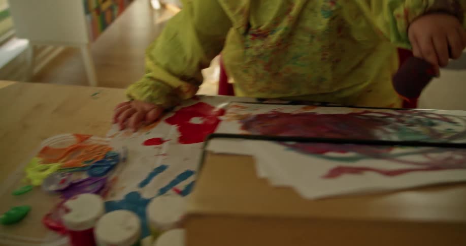 A little girl is painting using a sponge brush onto paper on an easel inside of a home during the day