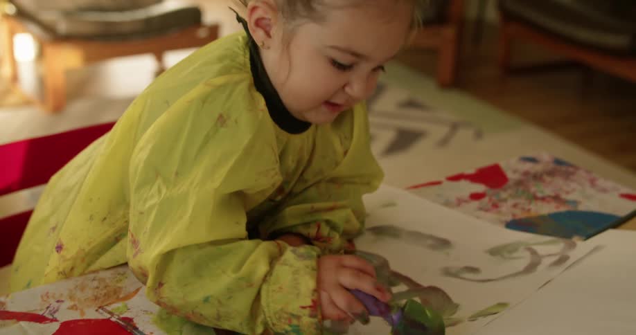 A child in a room sitting on a chair at a table painting on paper
