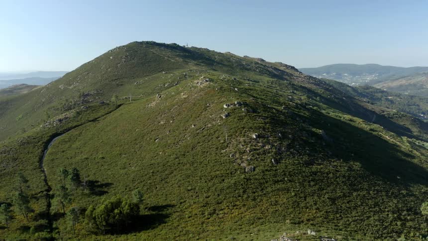 A hill with grass and trees with the sky and clouds in the background