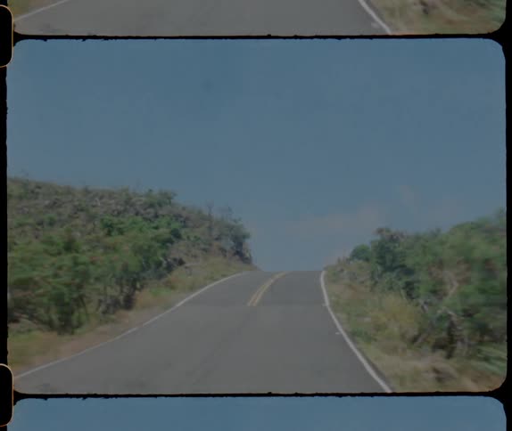 Car driving on a road through the hills caught on vintage film