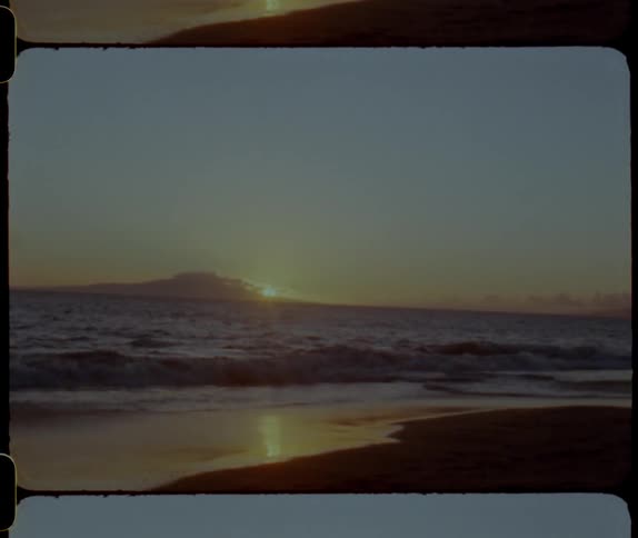 Ocean waves break against the shore and the beach is silhouetted against the sunset