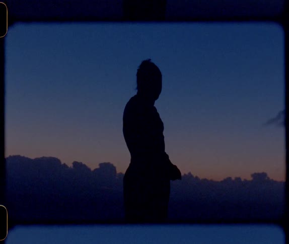 A vintage film of a person standing outside looking around as the sun sets