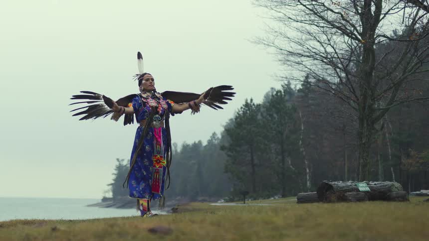 A native american woman is dancing in a tribal dress and bird feathers