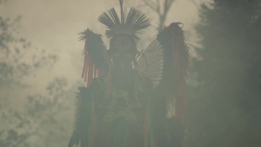 Smoke billows past a native man dressed in full ceremonial garb