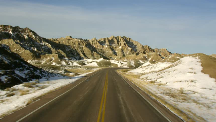 A road surrounded by mounds with a mountain range the sky and clouds in the background