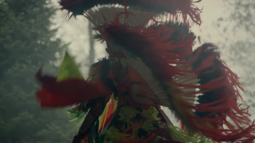 A native american man wearing tribal clothing is spinning and dancing outdoor