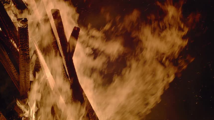 Flames smoke and embers against a night sky as wood burns
