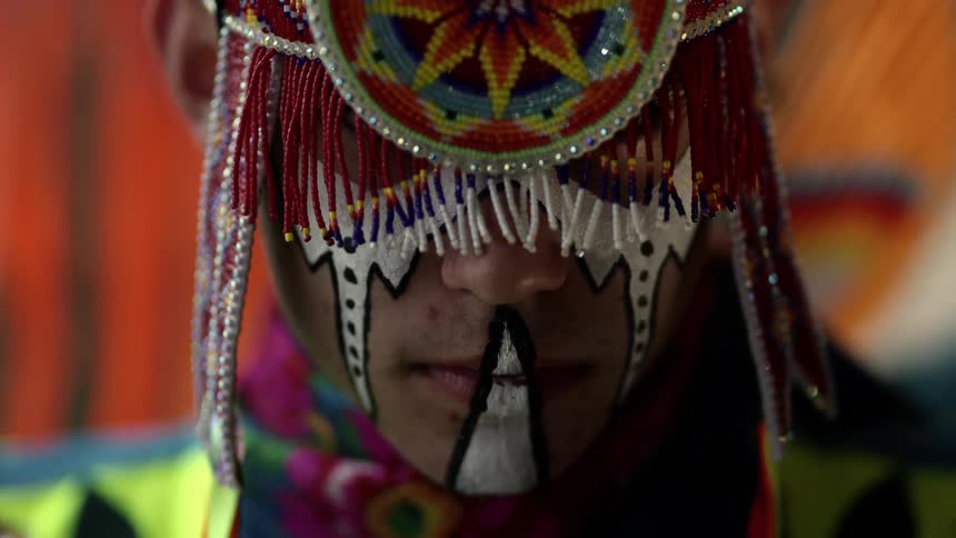 A man in a traditional mask with a wall in the background
