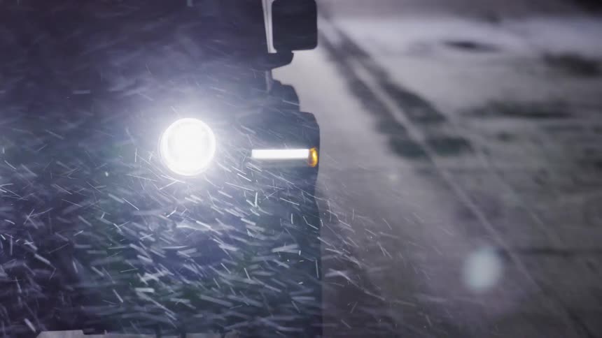 A vehicle travels down a road during a snowstorm at night