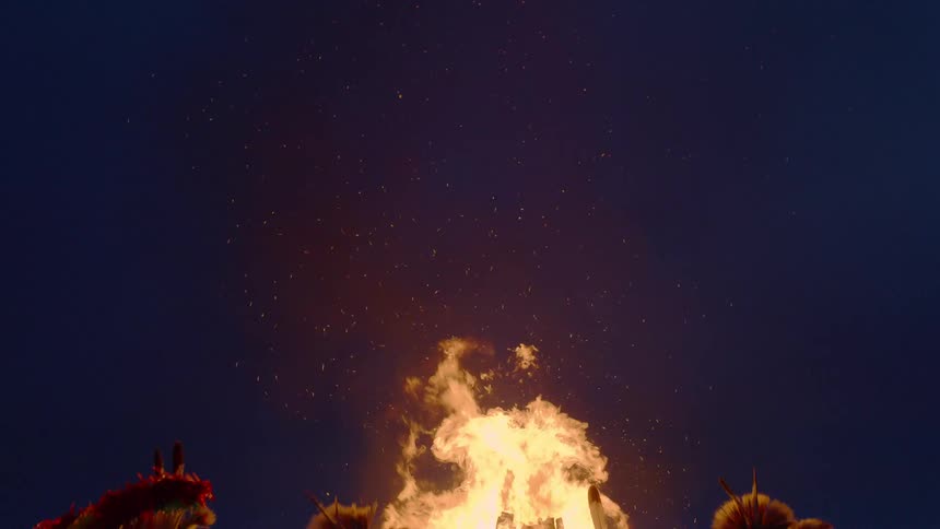 Indigenous people in full ceremonial garb dance near a burning fire at night