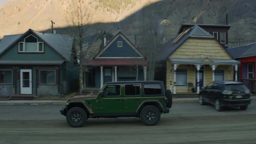 Man drives car through town in shadow as sun lights portion ofmountain in background