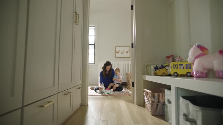 A woman sits on the floor at home and holds her baby as she plays with her