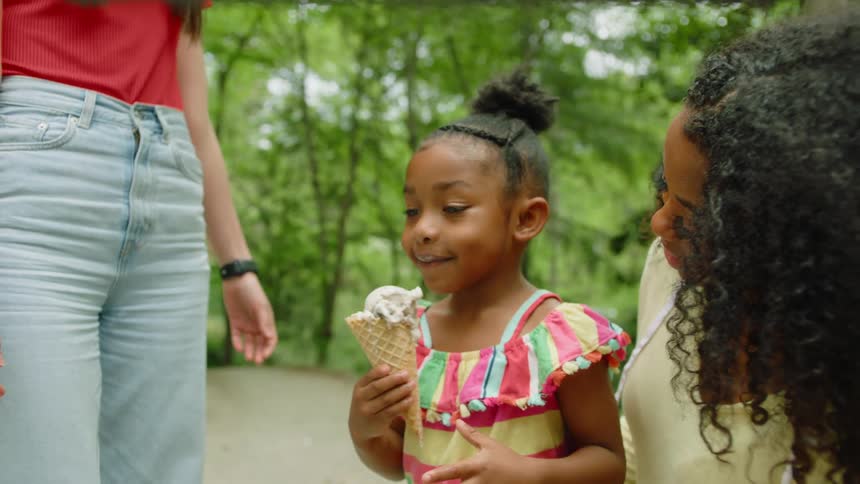 A little girl is eating ice cream outside next to her mother and another woman