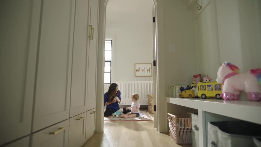 A woman is playing peekaboo and clapping with a baby in a sunny bedroom