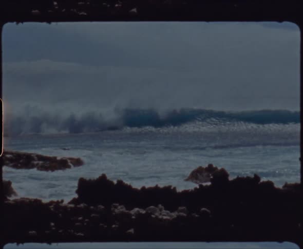 A large wave crashes on an empty rocky beach during the day
