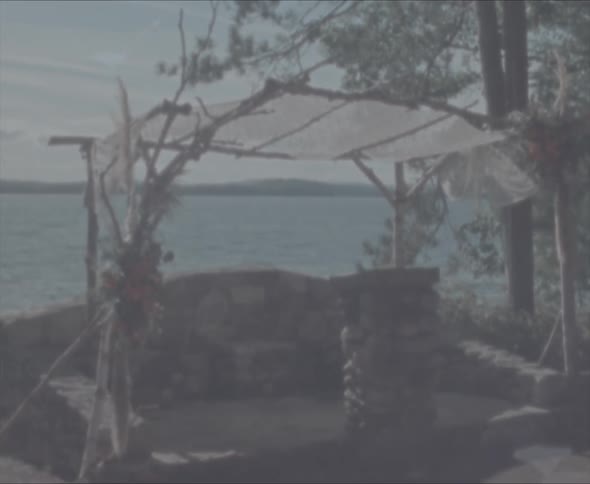 A makeshift shelter next to trees with a body of water the sky and clouds in the background