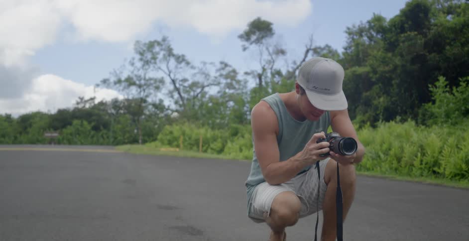 A man holding a camera squats down on a road