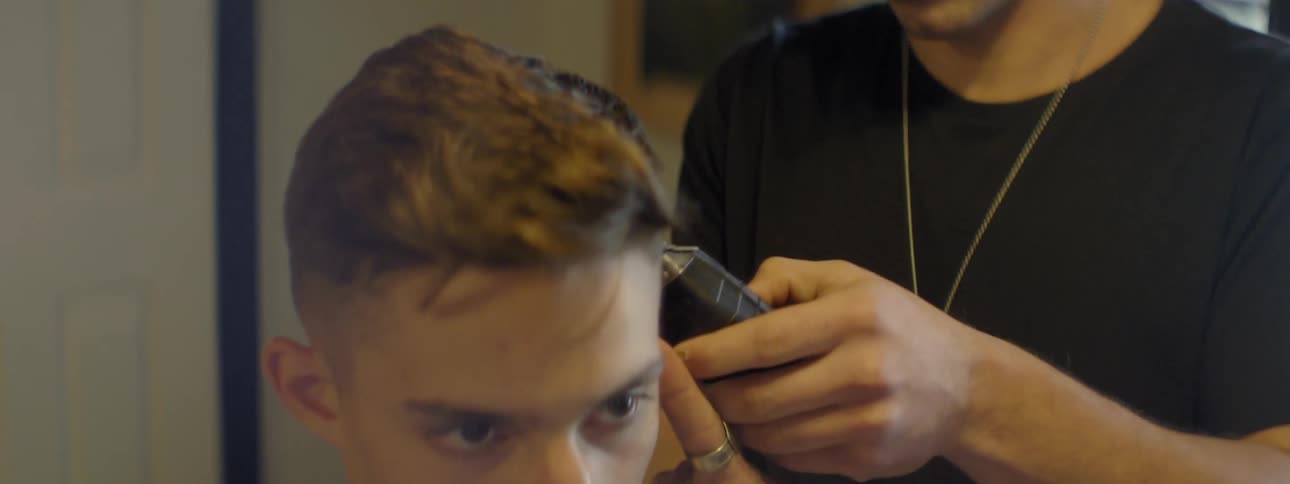 A barber uses an electric razor to cut a man's hair