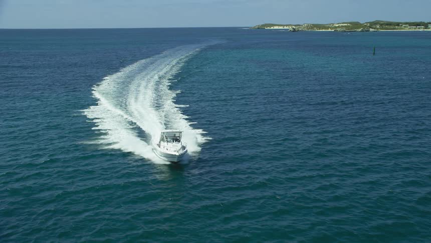 Small yatch navigating in the ocean near land leaving a white wake behind