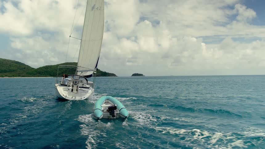 A sailboat moves through choppy water near a coast