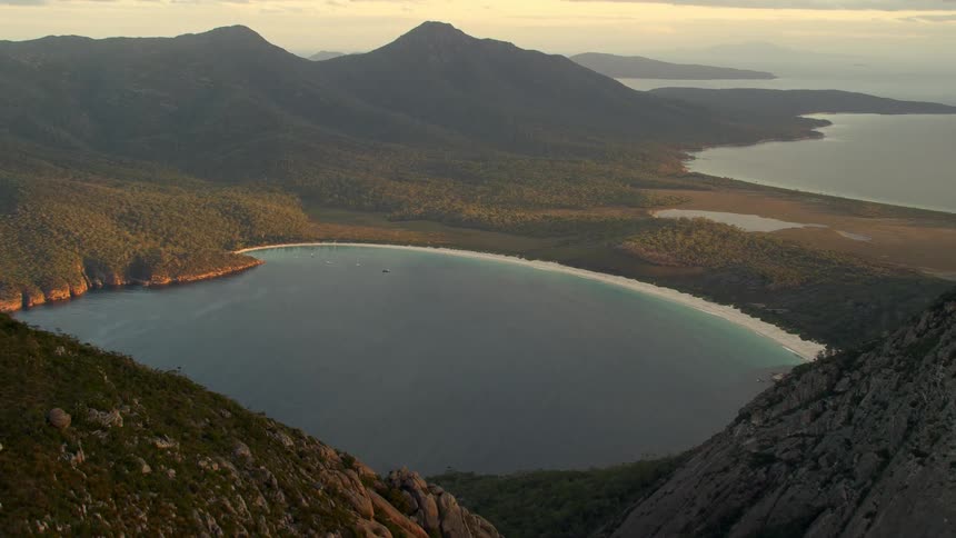 A lake surrounded by mountains and trees with the sky and clouds in the background