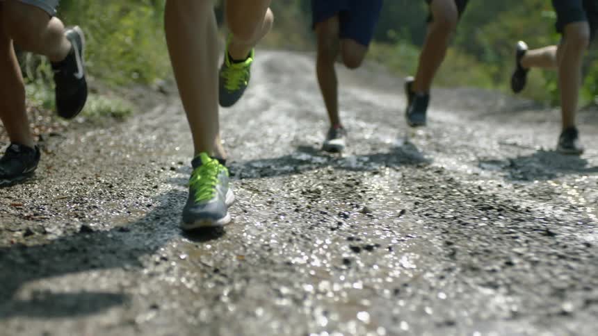 People with sneakers running on a wet dirt road with water and mud