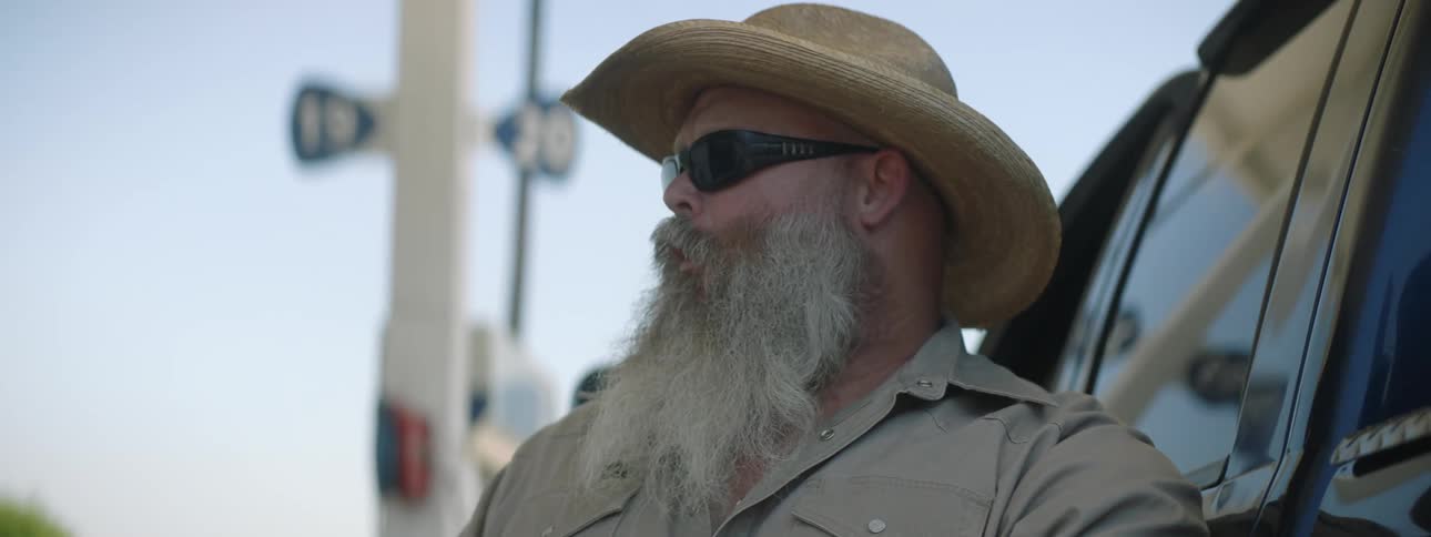 A man with a beard is eating food while pumping gas into his car at a gas station