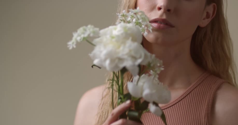 A young, blonde white woman holding a small bouquet of white flowers.