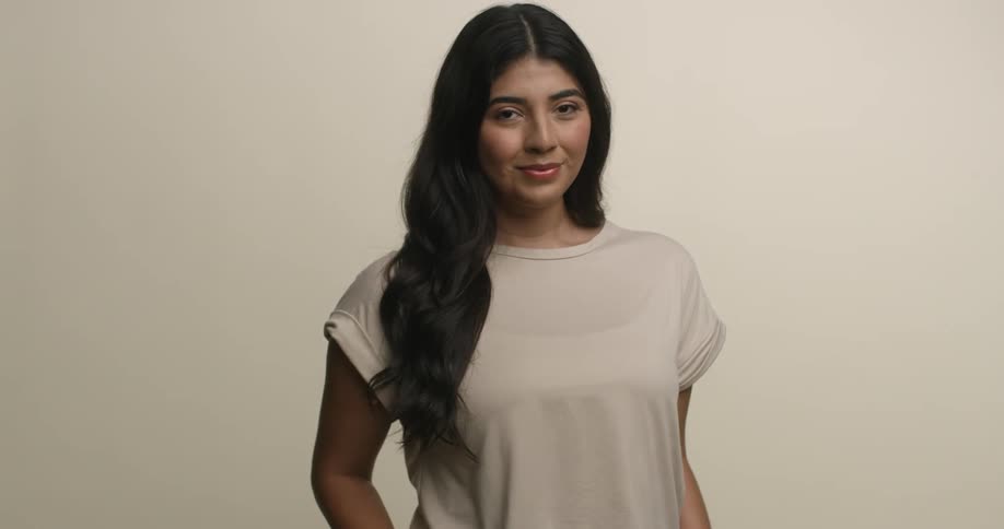 A young and exotic female model with long black hair stands and poses with a slight smile while looking into the camera