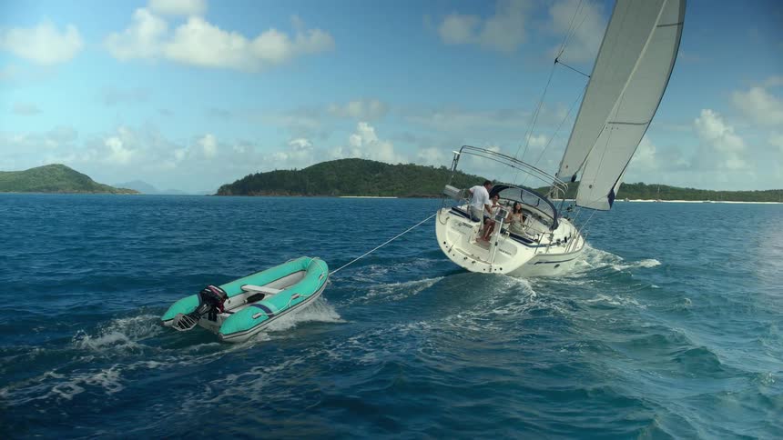 Sailboat carrying an inflatable raft on the ocean near islands