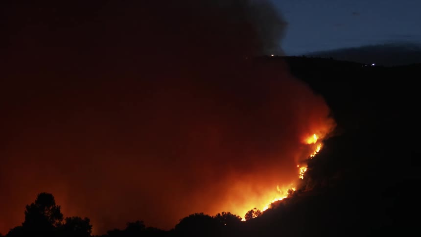 Aerial view of wildfire spreading and destroying the forest at night