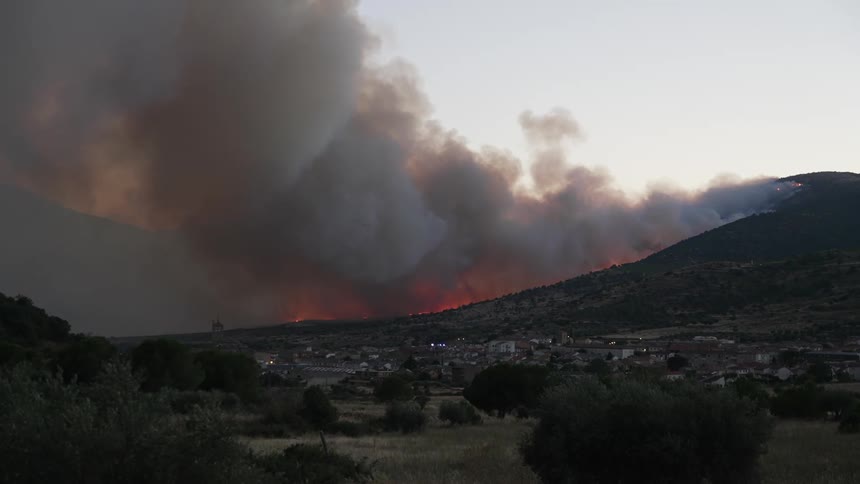 A hill the fire and smoke with the sky and clouds in the background