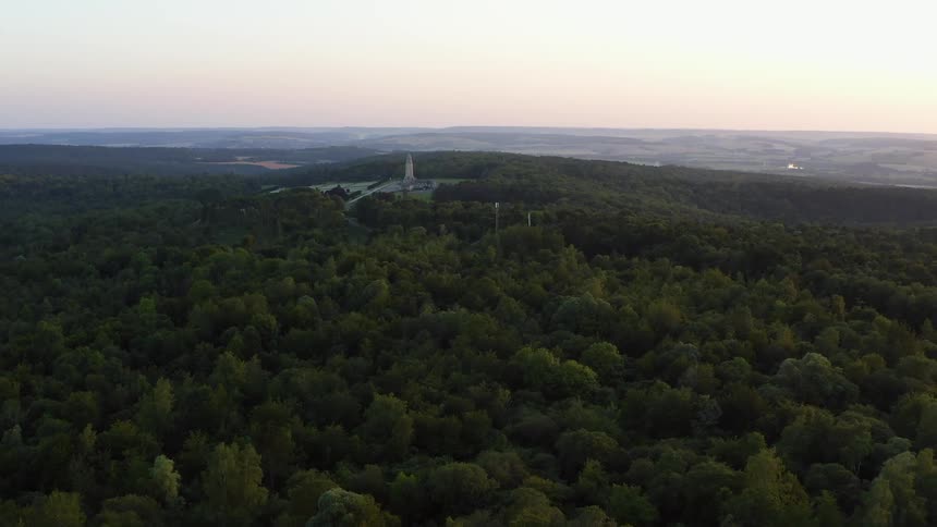 An aerial view of a tower on a hill surrounded by dense trees at dawn