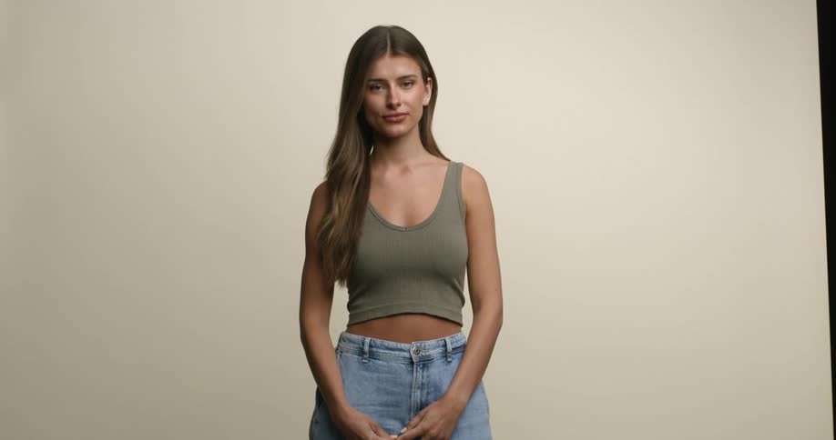 A young, white female model with long hair stands with hands touching in front of her body as she poses for a portrait.