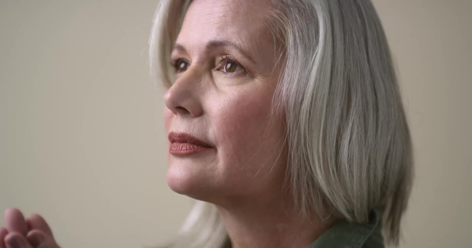 A close up of an older white female model with straight silver hair, dark eyes, and red lips as she gazes in to the distance