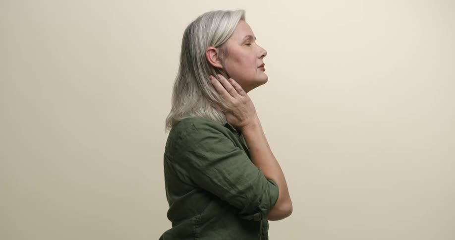 A mature woman in profile pushes her gray hair behind her ear with her hand and looks up at something in the distance.