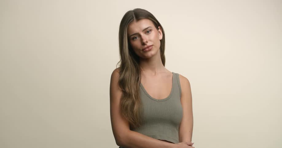 A teenage Caucasian female model tucks her chin and gives a pinched smirk then opens her lips and looks down her nose toward the camera