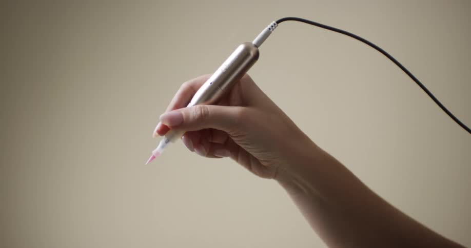 A manicured woman's hand holding and preparing to use an electric microblading pen.