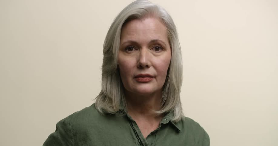 An older Caucasian woman with dark eyes and gray hair looks up and then back down to the camera