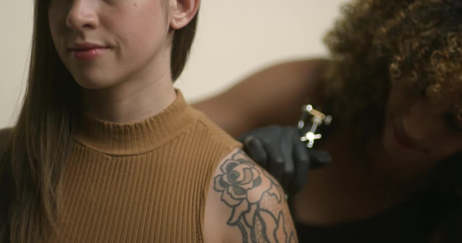 A young, caucasian woman getting inked by an ethnic, female tattoo artist.