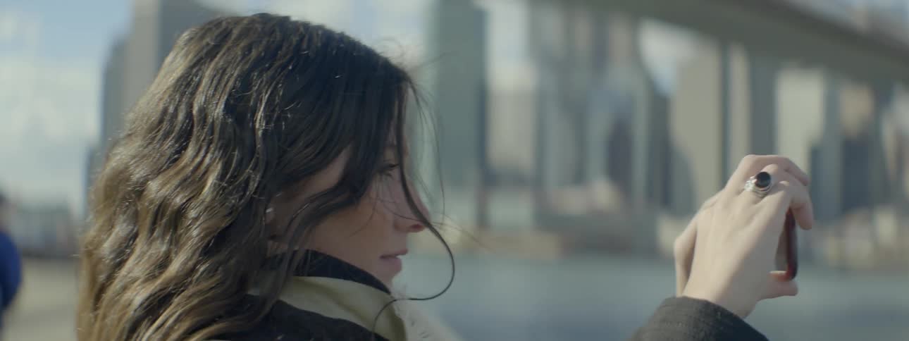 A woman raises a camera in front of her and turns to film a city view