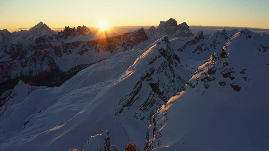 The sun is low in the sky over some snowy mountains