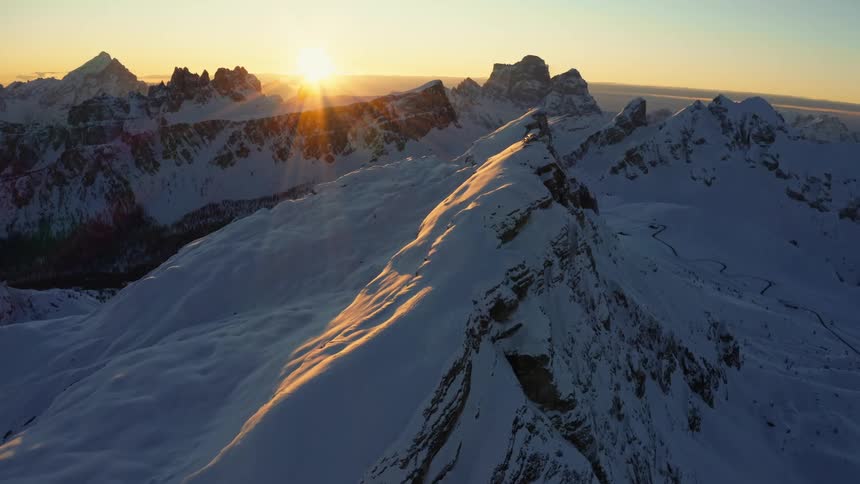 The sun rising over a snowy mountain range in the wilderness on a clear winter morning