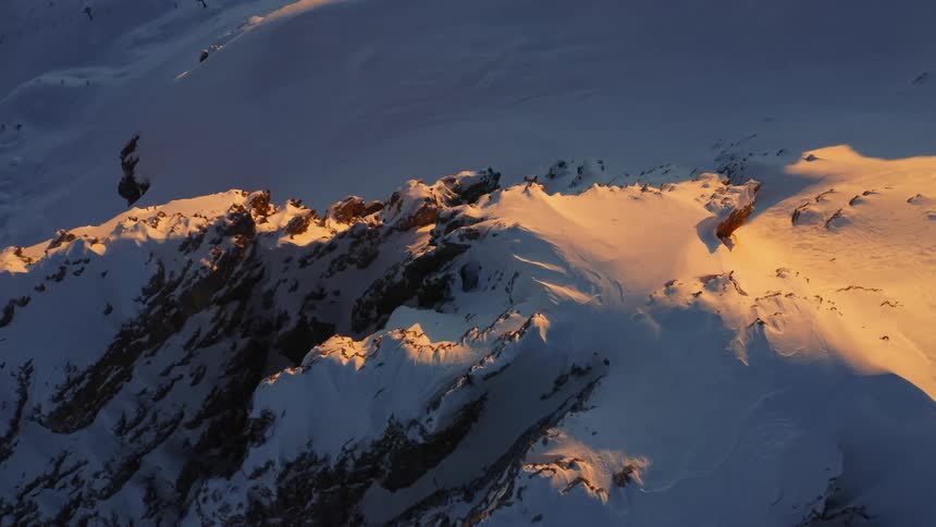 The sun shines on a snow covered mountain ridge