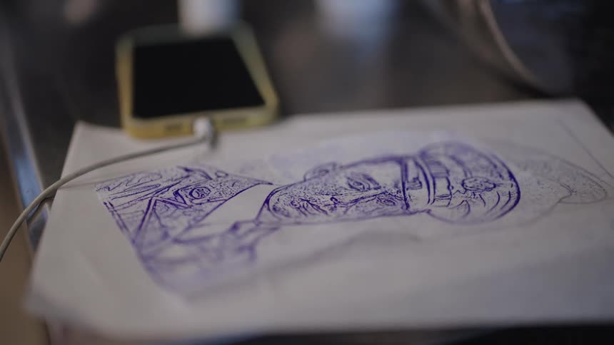 A drawing of a forlorn soldier in blue ink sits on a wood table next to a charging smartphone
