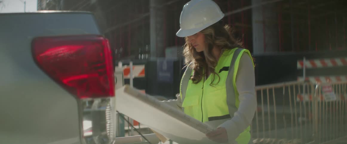 A female construction worker is outside at a site looking at building plan drawings