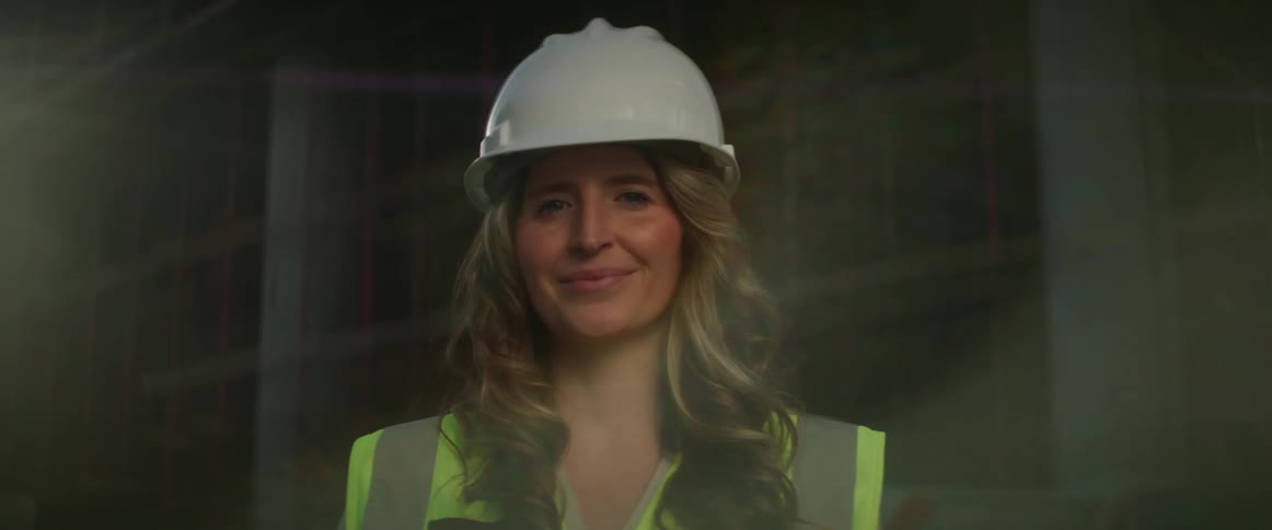 Female construction worker wearing hardhat stands near building under construction