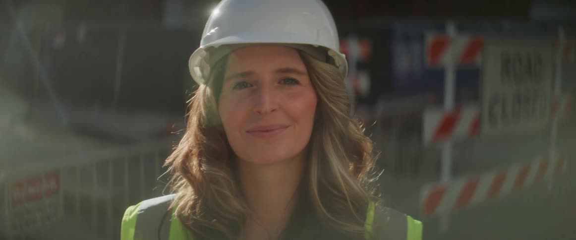 Female construction worker wearing a white hardhat looking at the camera near a construction site
