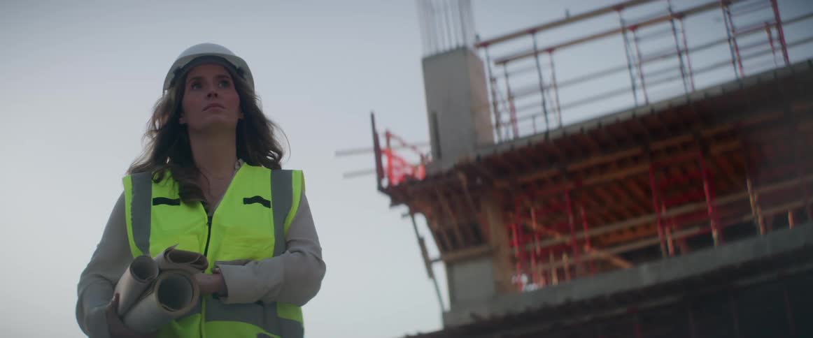 Woman walks past building under construction carrying rolled construction plans